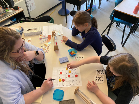 Two students and a teacher working on math together at a desk.